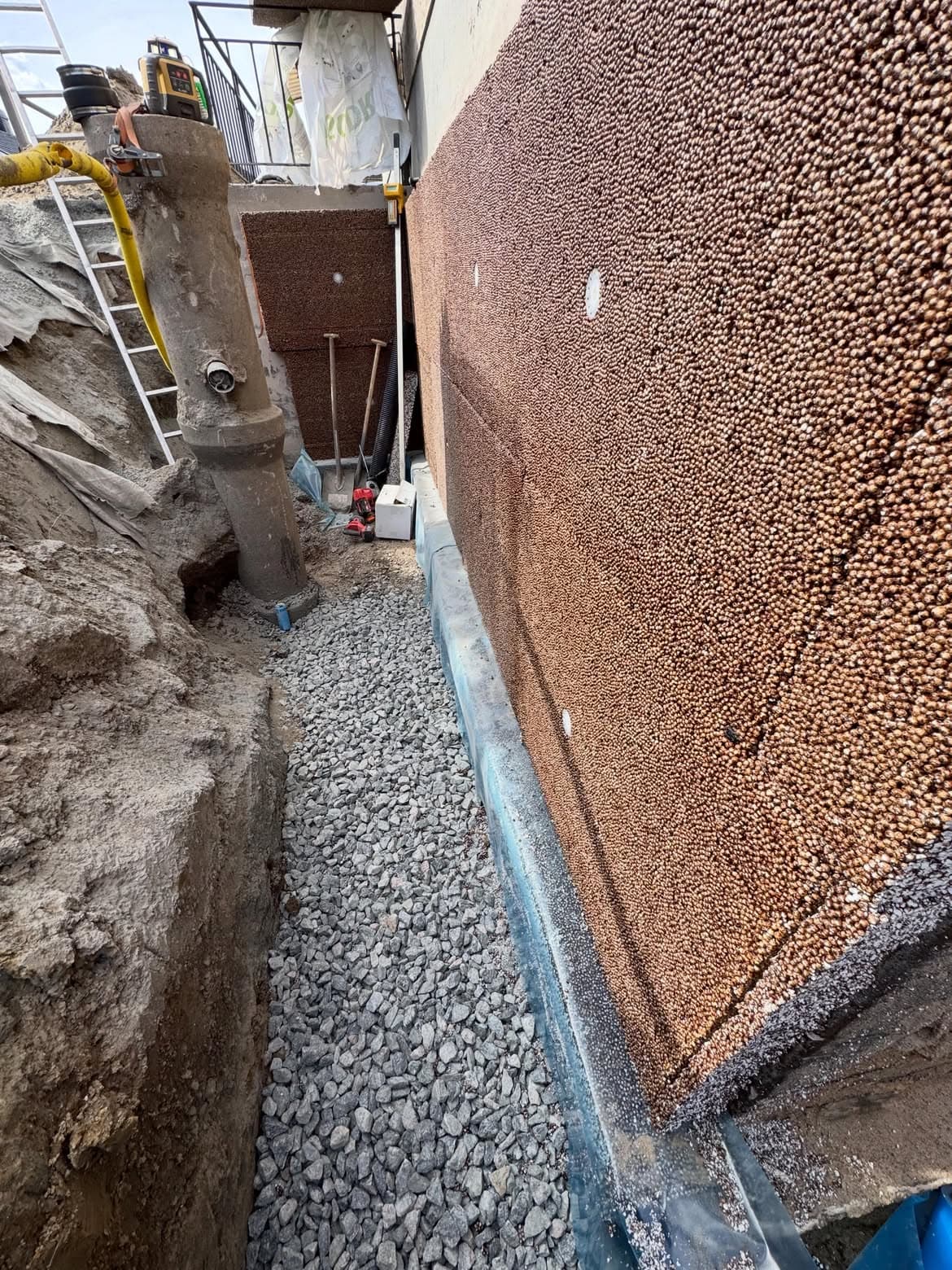 Isodränskivor och makadam längs källarväggen med ny dagvattenbrunn
