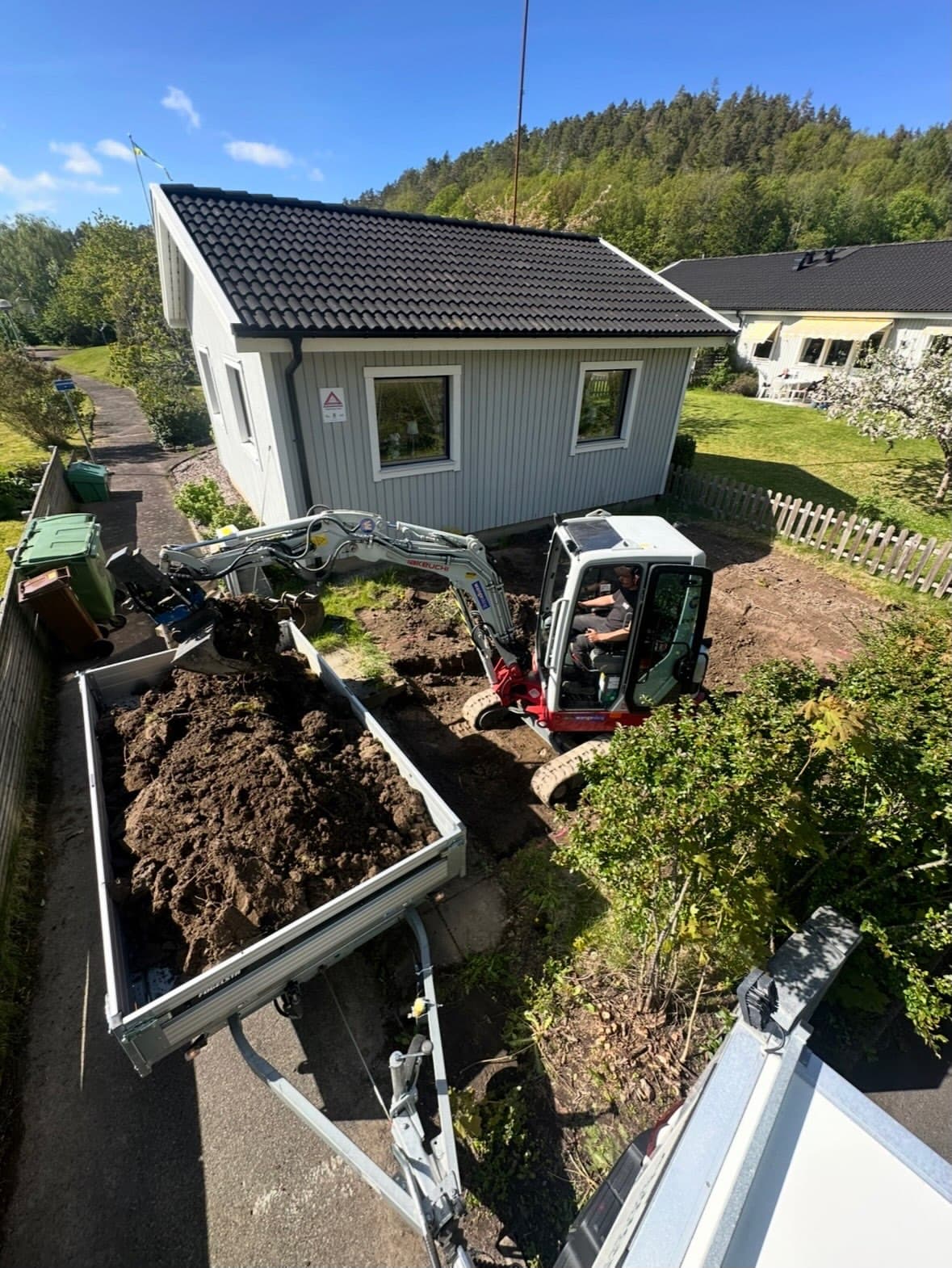 Grävmaskin utför grundarbetet för sopkärlsrummet vid BRF-huset