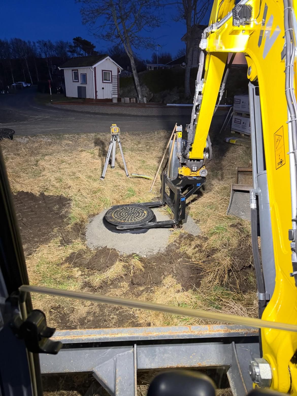 Nytt brunnslock sätts på plats med grävmaskin och rotationslaser