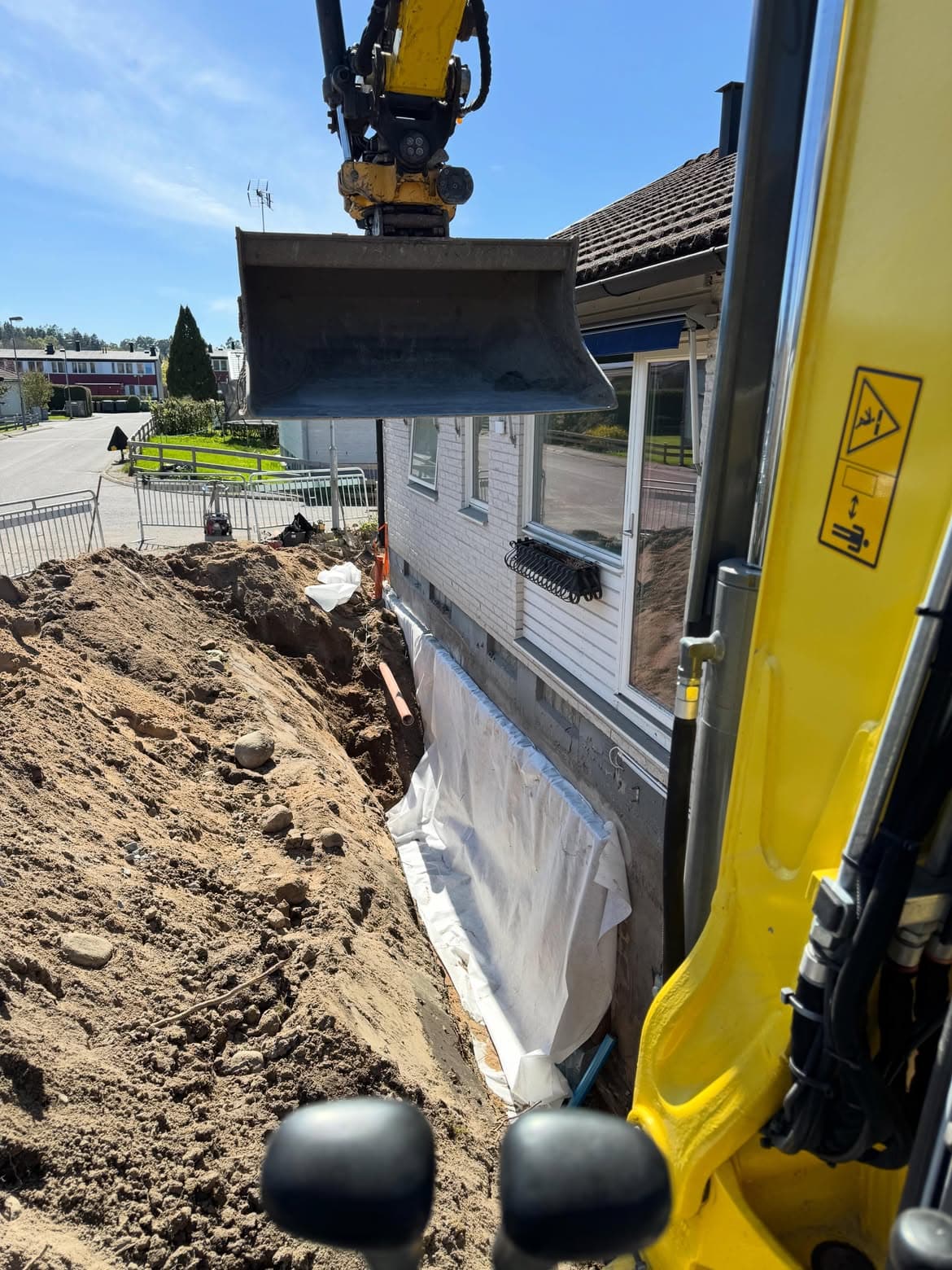 Grävmaskin återfyller schaktet längs husfasaden