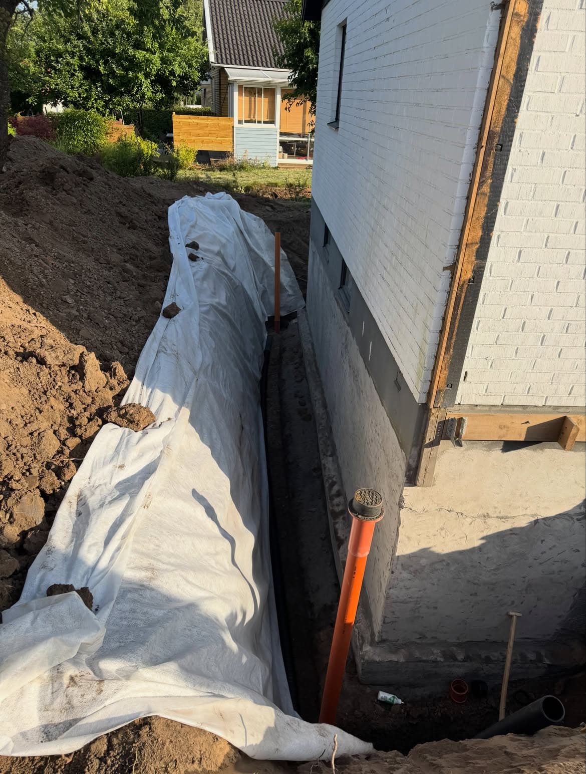 Dräneringsschakt med fiberduk längs husgrunden och uppstigningsrör för dagvatten
