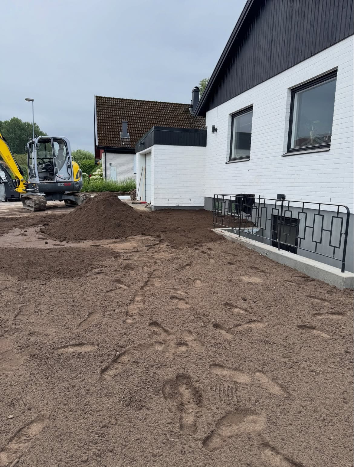 Minigrävare planerar ut ny matjord framför huset